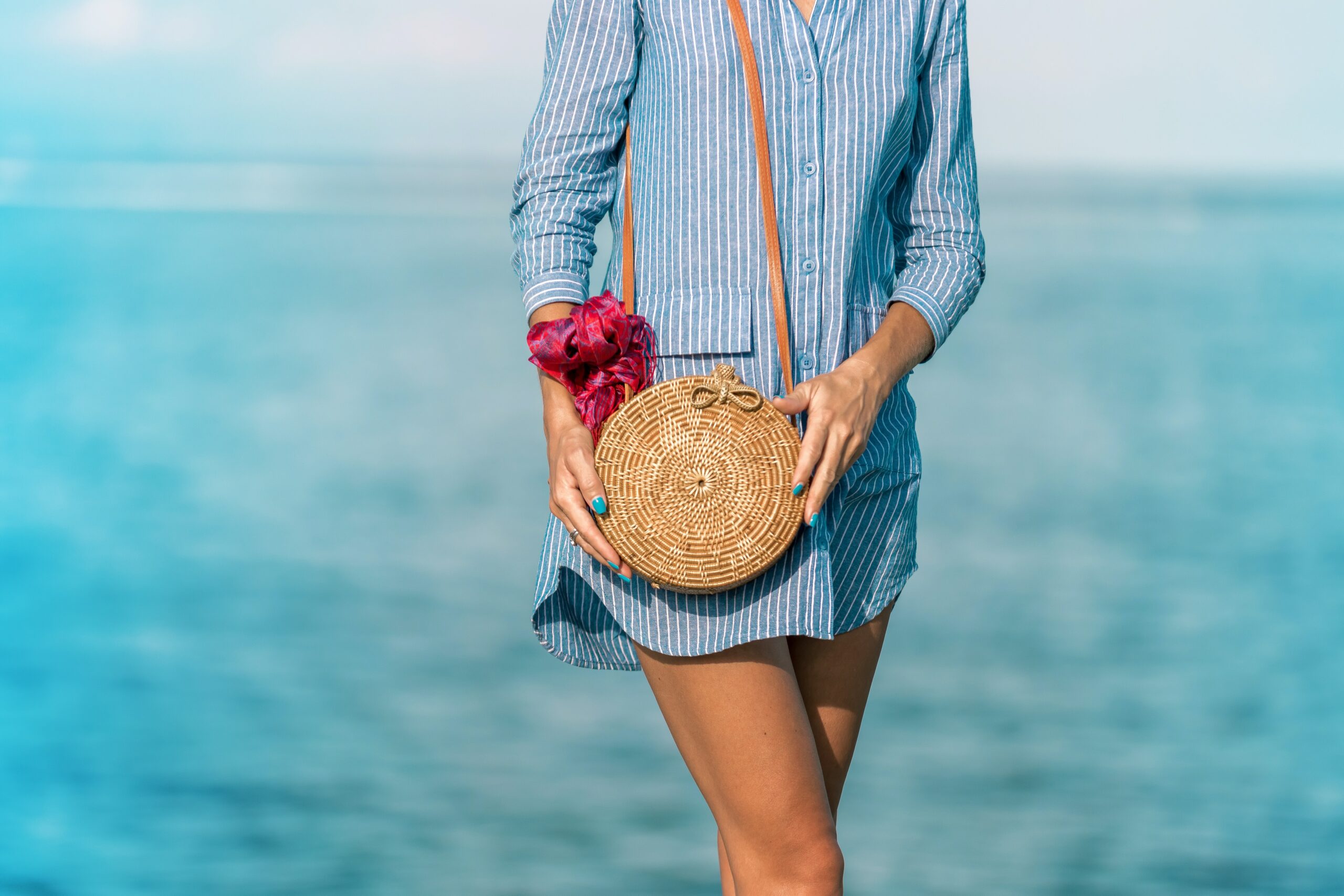 woman wearing blue and white striped dress shirt dress with brown wicker crossbody bag near sea at daytime